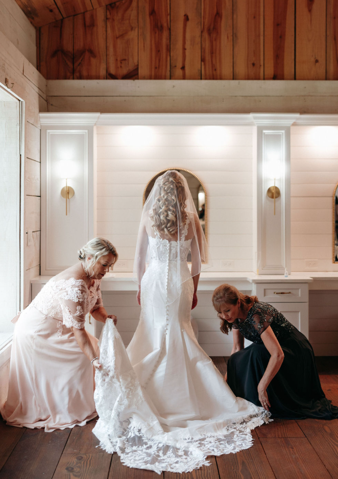 Bride having dress train laid out by mother and mother in law.